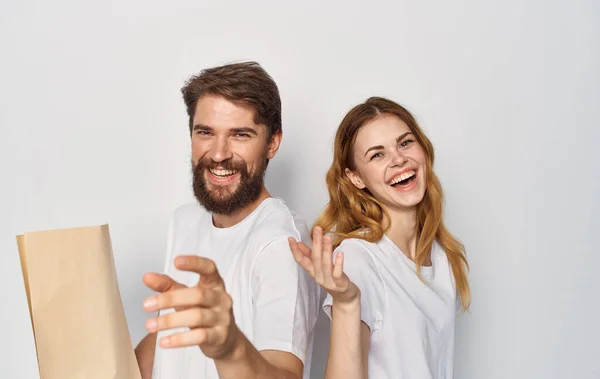 Χαρούμενο νεαρό ζευγάρι σε λευκό T-shirts πακέτο με παντοπωλεία τρέχει αντίχειρα επάνω — Φωτογραφία Αρχείου