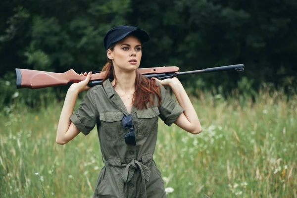 Militar mulher segurando uma arma atrás de suas costas black cap caça estilo de vida macacão verde — Fotografia de Stock