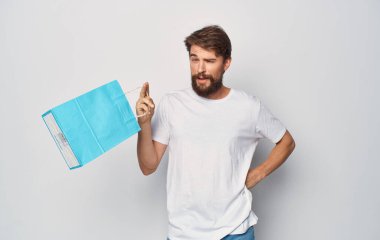 Beyaz tişörtlü sakallı bir adam elinde bir paketle alışverişe çıkıyor.