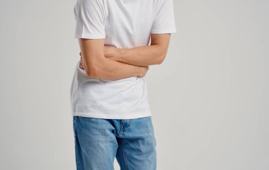 Beyaz tişörtlü ve kot pantolonlu bir adam elleriyle karnına dokunuyor.