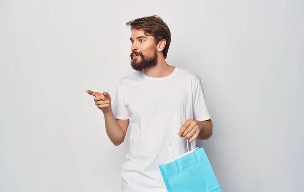 Homem barbudo em uma camiseta branca com um pacote em sua mão Compras divertido isolado fundo — Fotografia de Stock