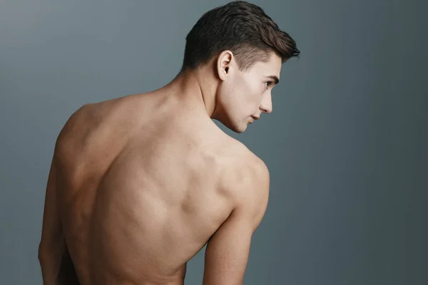 Sexy man met een naakte rug kijkt naar de zijkant op een grijze achtergrond achteraanzicht van een fitness sport model — Stockfoto