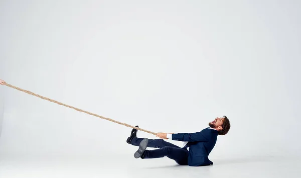 A business man lies on the floor and pulls a rope on a light background indoors — Stock Photo, Image