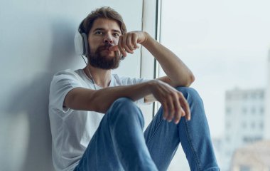 Kulaklık takan bir adam pencere pervazında oturur ve araba direksiyonu sürerken taklit müzik dinler.