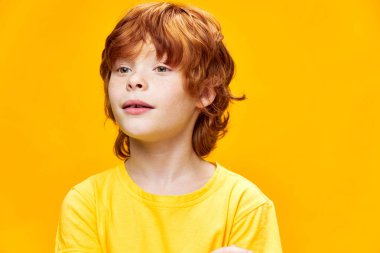 Sarı tişörtlü, kızıl saçlı çocuk yan yatmış, yakın çekime bakıyor. 