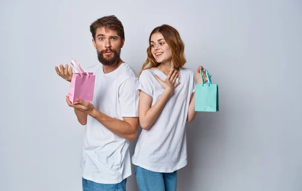 Muž a žena s dárkovými taškami stojí jeden k druhému na šedém pozadí — Stock fotografie