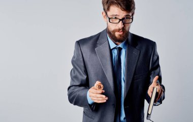 Elinde bozuk para ve gri arka planda ceketi olan bir işadamı elleriyle el kol hareketi yapıyor. 