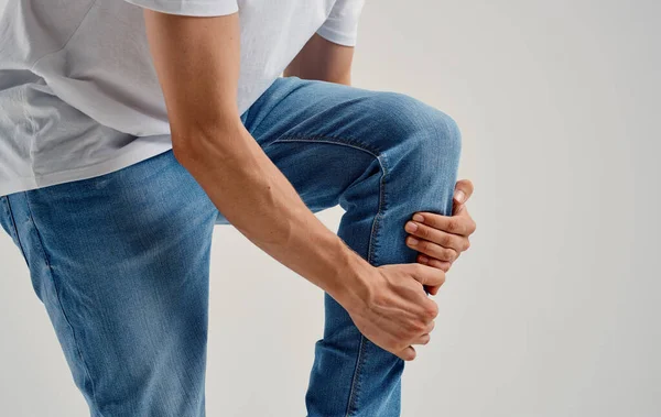 Человек в джинсах касается колена руками на светлом фоне обрезанный вид — стоковое фото