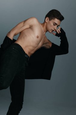 Gri arka planda takım elbiseli yakışıklı bir adam tek bacağının üzerinde duruyor ve yana doğru eğiliyor.