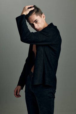 Siyah ceketli bir adam elini kafasında tutarak moda yapıyor.