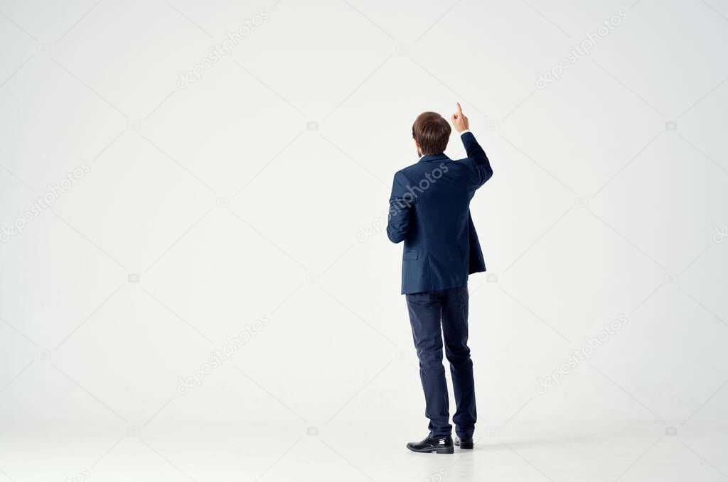 Gentleman in a blue suit gestures with his hands on a light background back view business finance