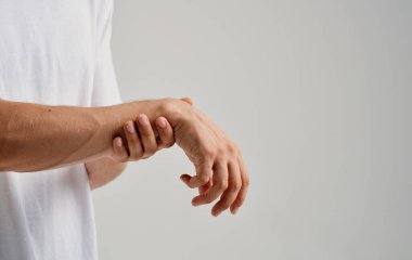 Beyaz tişörtlü bir adam hafif arka planda bileklerine dokunuyor.