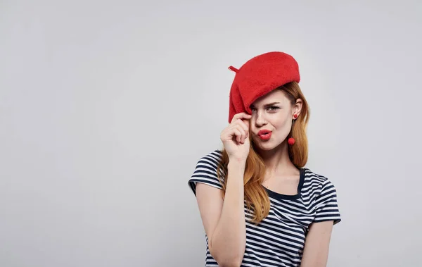 Donna in t-shirt a righe tocca cappello rosso sulla sua testa luce sfondo vista ritagliata — Foto Stock