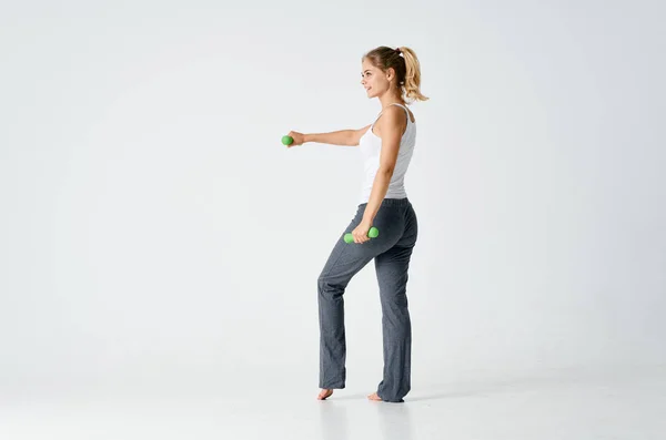 Mujer entra para los deportes con pesas en una habitación luminosa y pantalones grises —  Fotos de Stock