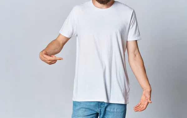 Un hombre con una camiseta blanca sobre un fondo claro gestos con las manos recortadas vista de jeans Copiar espacio —  Fotos de Stock