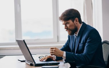 Şaşkın iş adamı ofis ofis modelinin masasındaki dizüstü bilgisayara bakar.