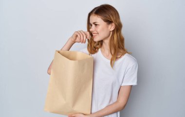 Beyaz tişörtlü ve kotlu bir kadın elinde paketle markete gidiyor.