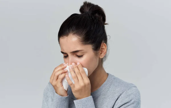 Donna soffia il naso in un tovagliolo naso che cola problemi di salute sfondo grigio — Foto Stock