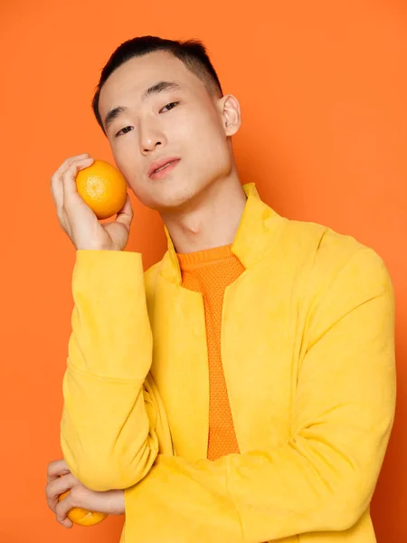 Young man with orange in hand and yellow jacket isolated background cropped view — Stock Photo, Image
