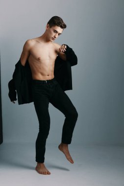 Pantolon giyen bir adam gömleğini kapalı alanda gri arka planda çıkartıyor.