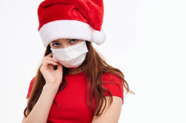 Noel Baba şapkası takan kırmızı tişörtlü, tıbbi maske takan bir kız.