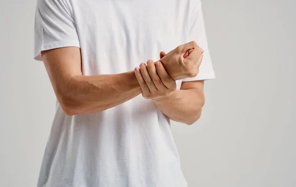 Ein Mann im weißen T-Shirt berührt seine Handgelenke vor hellem Hintergrund — Stockfoto