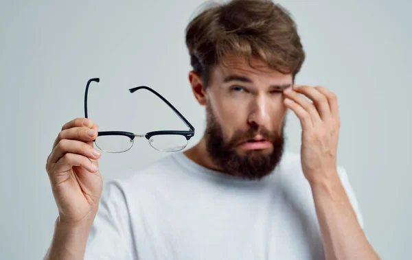 눈이 좁은 남자가 가벼운 배경 시력 문제에 대해 손에 안경을 쥐고 있다 — 스톡 사진