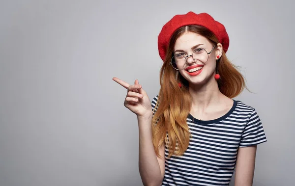 Mujer emotiva en gafas y en una camiseta a rayas gestos con sus manos sombrero rojo — Foto de Stock