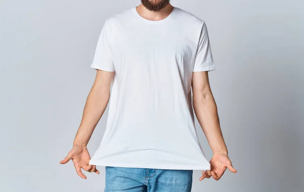 Um homem em uma camiseta branca em um fundo leve gesticula com as mãos vista cortada de jeans espaço de cópia — Fotografia de Stock