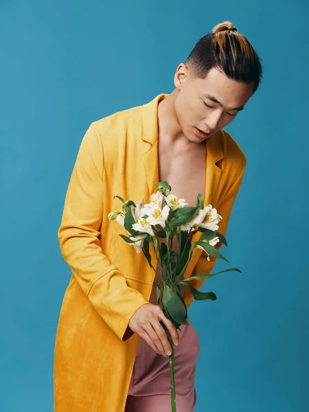 黄色のコートを着たファッショナブルな男は、青い背景に白い花の花束を手に取ります — ストック写真