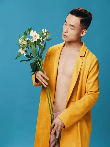 青い背景に白い花の花束を持つ黄色のコートのハンサムな男 — ストック写真