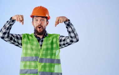 Miğferli bir inşaat işçisi elleri ve yansıtıcı yeleği ile hareket eder.