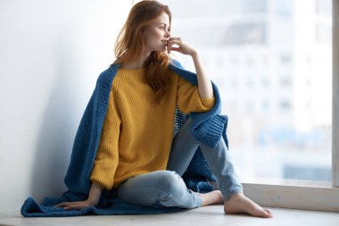 Ekoseli güzel bir kadın pencere eşiğinde oturur ve pencereden dışarı bakar.