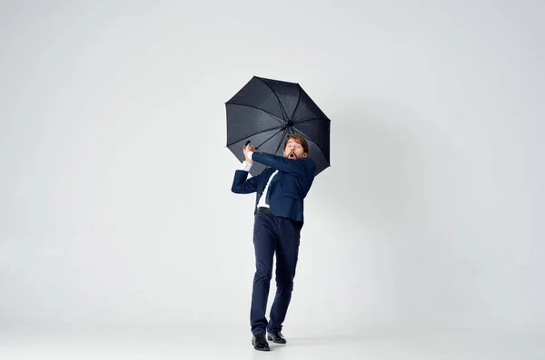 Бизнесмен в костюме позирует на светлом фоне с черным зонтиком в руке — стоковое фото