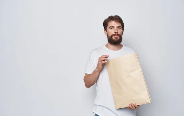 Емоційний чоловік у білій футболці з ремісничим пакетом в руках емоцій студії ізольований фон — стокове фото