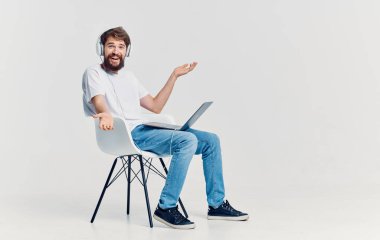 Kulaklıklı, dizlerinin üstünde dizlerinin üstünde oturan ve arka planda izole bir şekilde oturan bir adam.