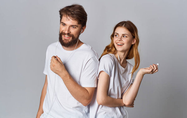 happy man and woman in headphones on gray background look and stand with their backs to each other
