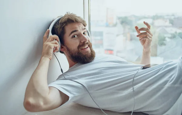 Mężczyzna w słuchawkach słuchanie muzyki reszta w pobliżu wnętrza okna — Zdjęcie stockowe