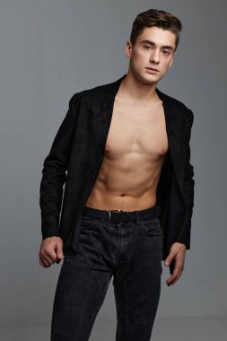 Düğmesiz ceketli ve pantolonlu, gri arka planda seksi bir adam.