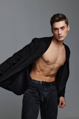 Düğmesiz gömlekli ve pantolonlu bir beyefendi gri arka planda yana doğru eğildi.