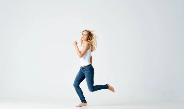 a slender woman in jeans and a white T-shirt barefoot on a light background in full growth