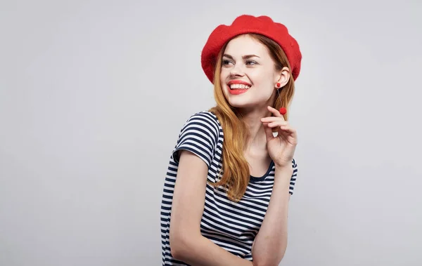 Modelo em chapéu vermelho e em uma camiseta listrada em um fundo leve emoções retrato recortado vista — Fotografia de Stock