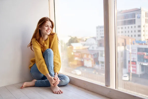 Mulher no peitoril da janela em um suéter amarelo e jeans estilo de vida de lazer — Fotografia de Stock