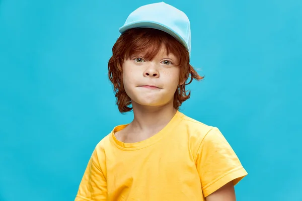 Rudowłosy chłopiec w czapce zapakował usta w żółty t-shirt niebieskie tło — Zdjęcie stockowe