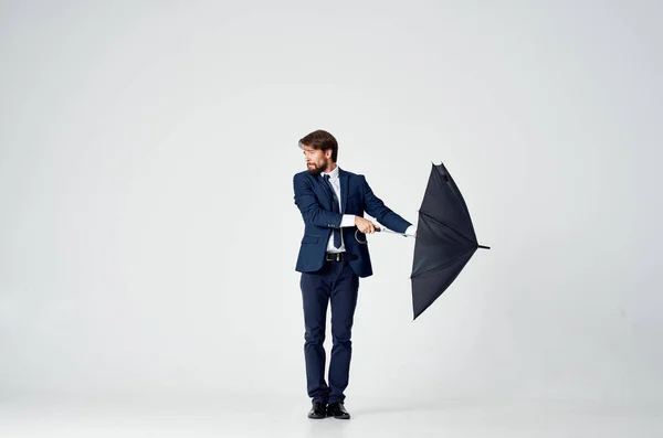 Homme d'affaires en costume posant sur un fond clair avec un parapluie noir à la main — Photo