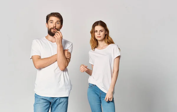 Un hombre y una mujer en jeans y una camiseta sobre un fondo claro gesticulando con las manos retrato amigos familia — Foto de Stock
