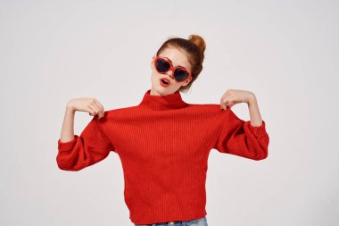 Hafif arka planda güneş gözlüklü şık bir kadın ve kırmızı kazak modeli makyajı.
