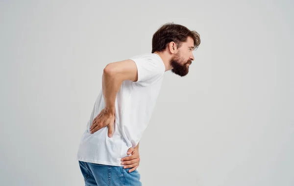 Un hombre con una camiseta blanca se toca la espalda con el dolor de la columna vertebral de la mano — Foto de Stock