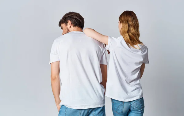 Un hombre y una mujer en las mismas camisetas y pantalones vaqueros están haciendo gestos con sus manos, vista trasera —  Fotos de Stock