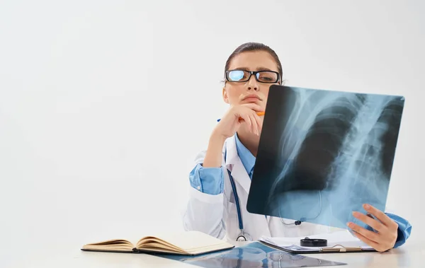 Доктор за столом з рентгенівським випромінюванням в руках і жінкою-моделлю запису книги — стокове фото